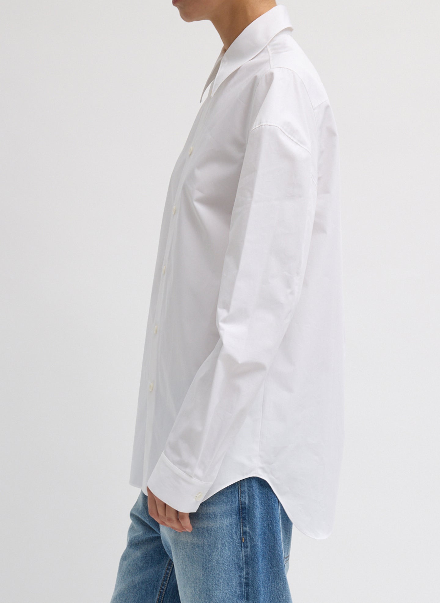 Side view of woman wearing Spring fashion in light wash jeans and Tibi White Compact Eco Poplin Hinged Shirt at Alas Eius 