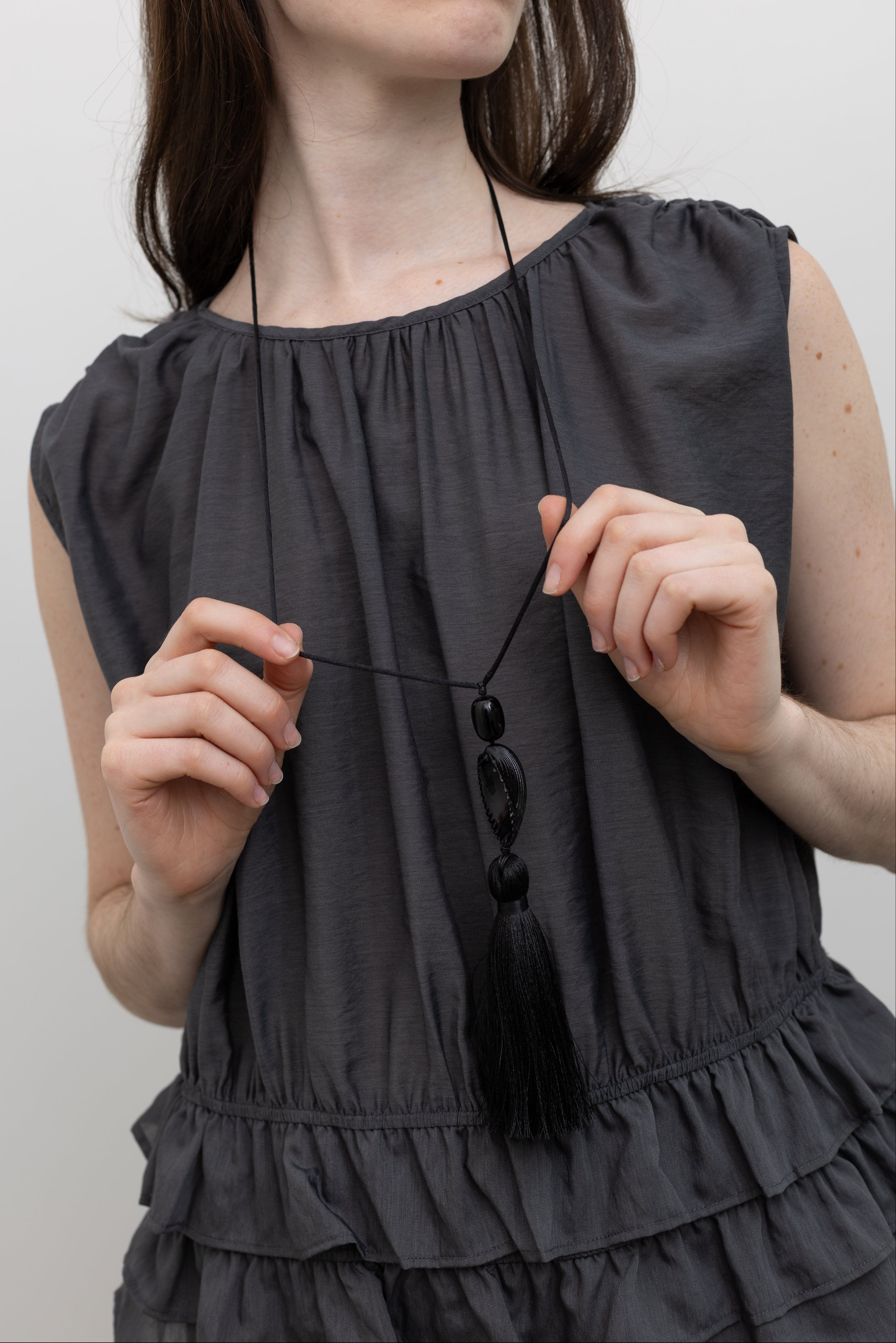 Coastal-inspired pendant necklace by Totore Studio showcasing a black seashell charm on an adjustable silk cord with a soft tassel finish at Alas Eius.