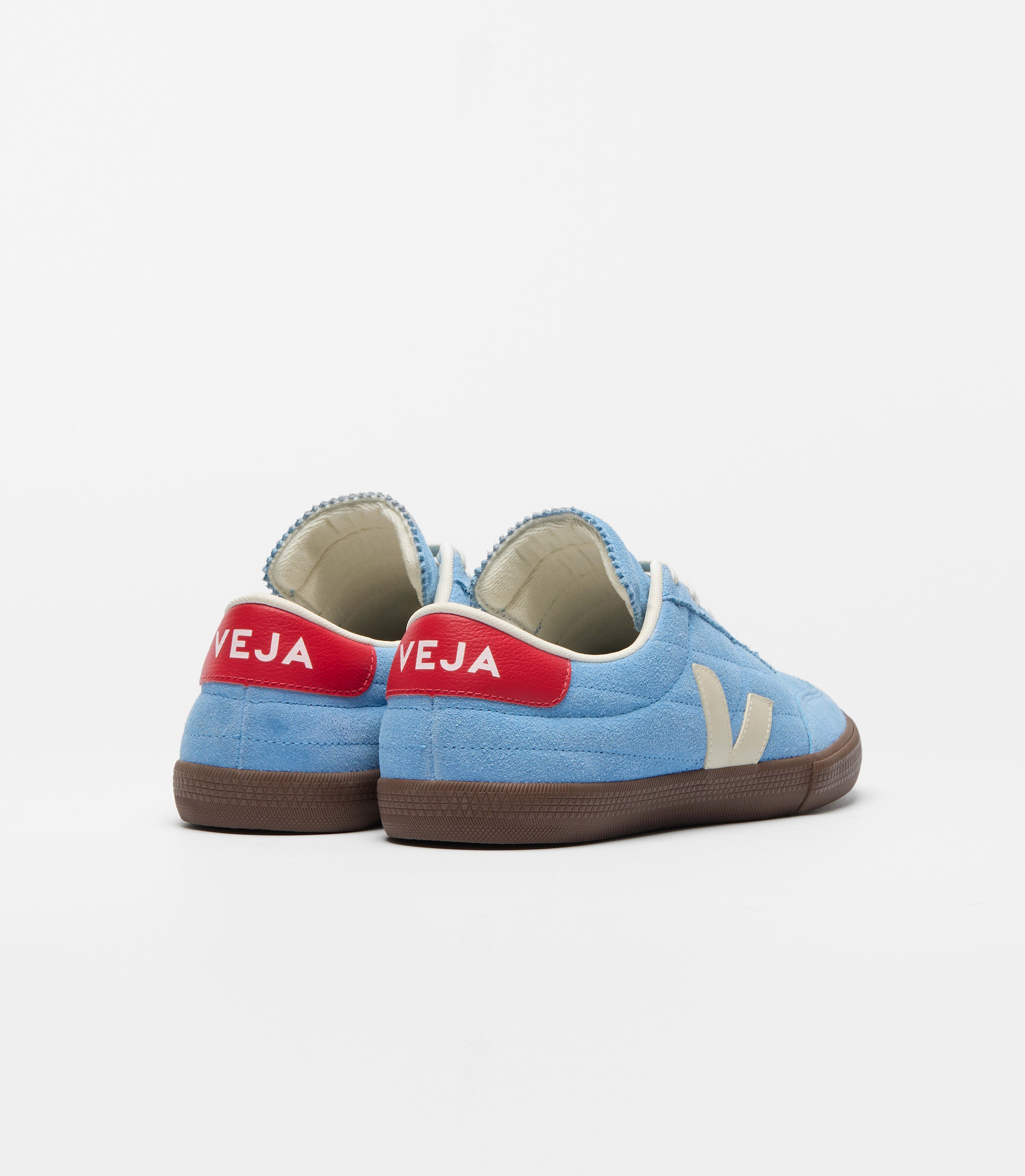 Back view of Veja sneakers in a sky blue suede upper paired with contrasting cream details and a rich brown sole. Finished with a bold red heel tab and signature side logo, the design blends sport and urban culture with modern everyday style at an Alas Eius store. 