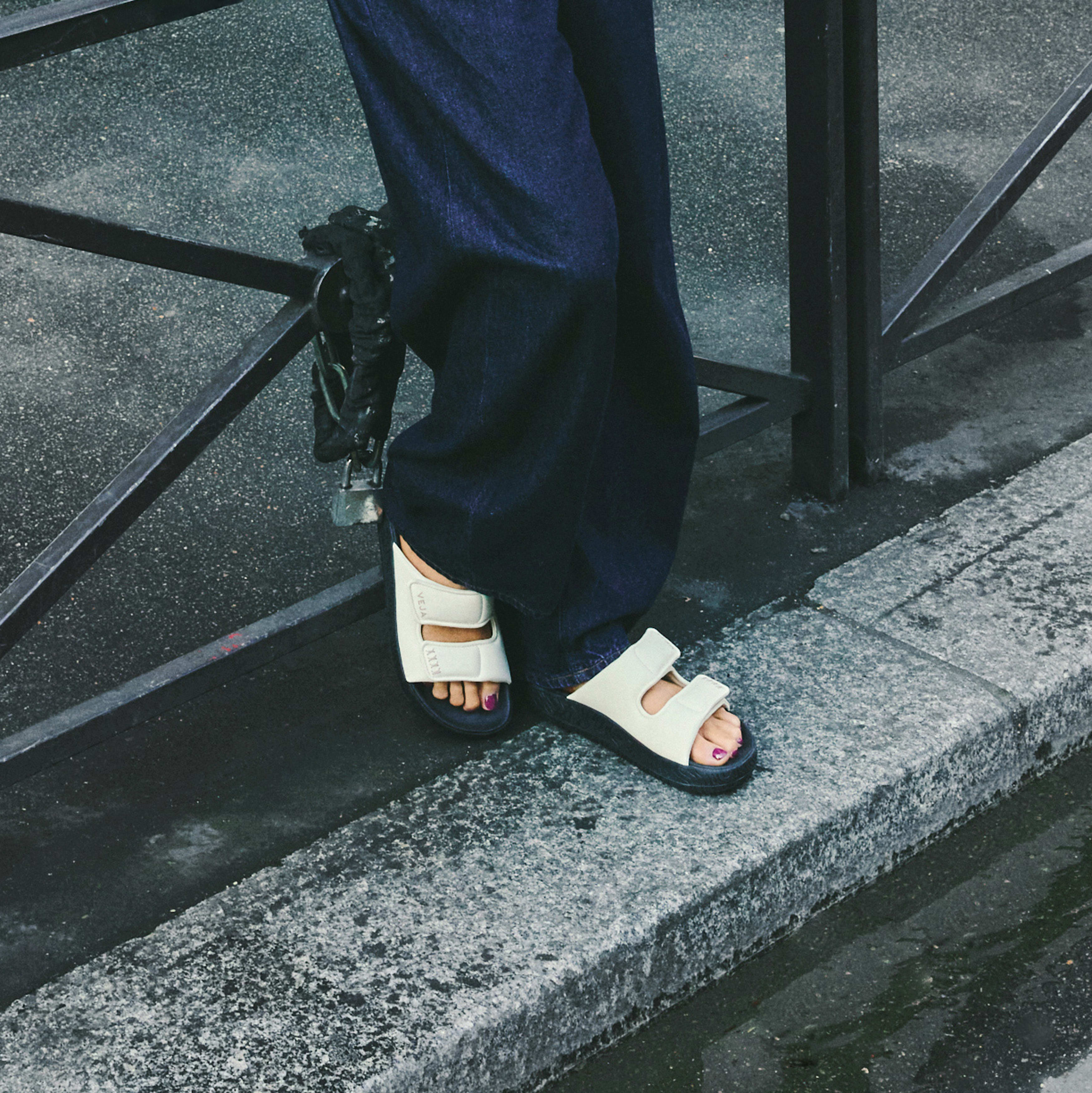 Woman wearing a sporty Veja sandal featuring a minimalist double-strap silhouette crafted in a soft cream leather and a bold black platform sole with dark wash denim jeans at an Alas Eius store. 