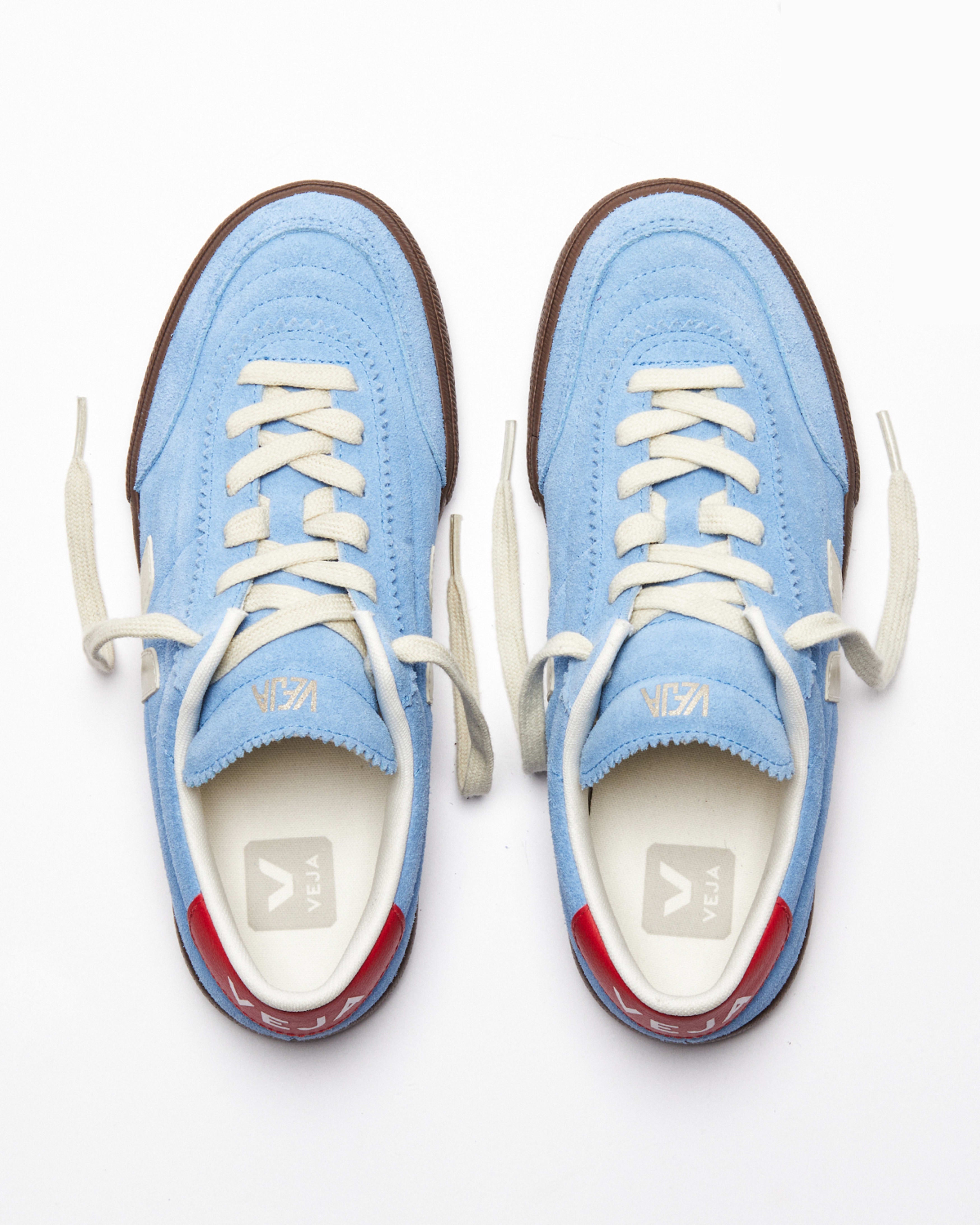 Overhead view of Veja sneakers in a sky blue suede upper paired with contrasting cream details and a rich brown sole. Finished with a bold red heel tab and signature side logo, the design blends sport and urban culture with modern everyday style at an Alas Eius store. 