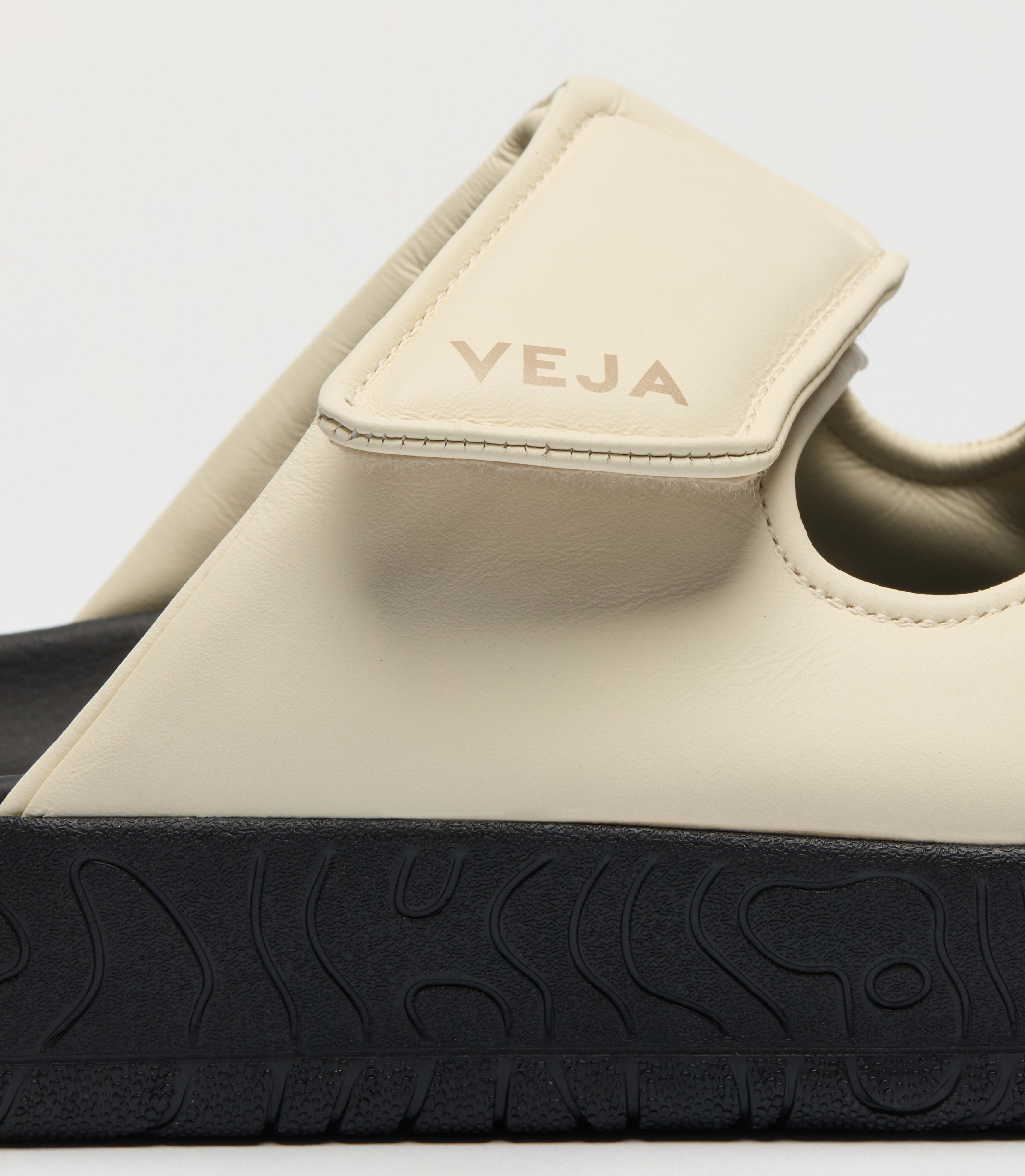 Close-up view of the Veja sandal featuring a minimalist double-strap silhouette crafted in a soft cream leather and a bold black platform sole at an Alas Eius store. 