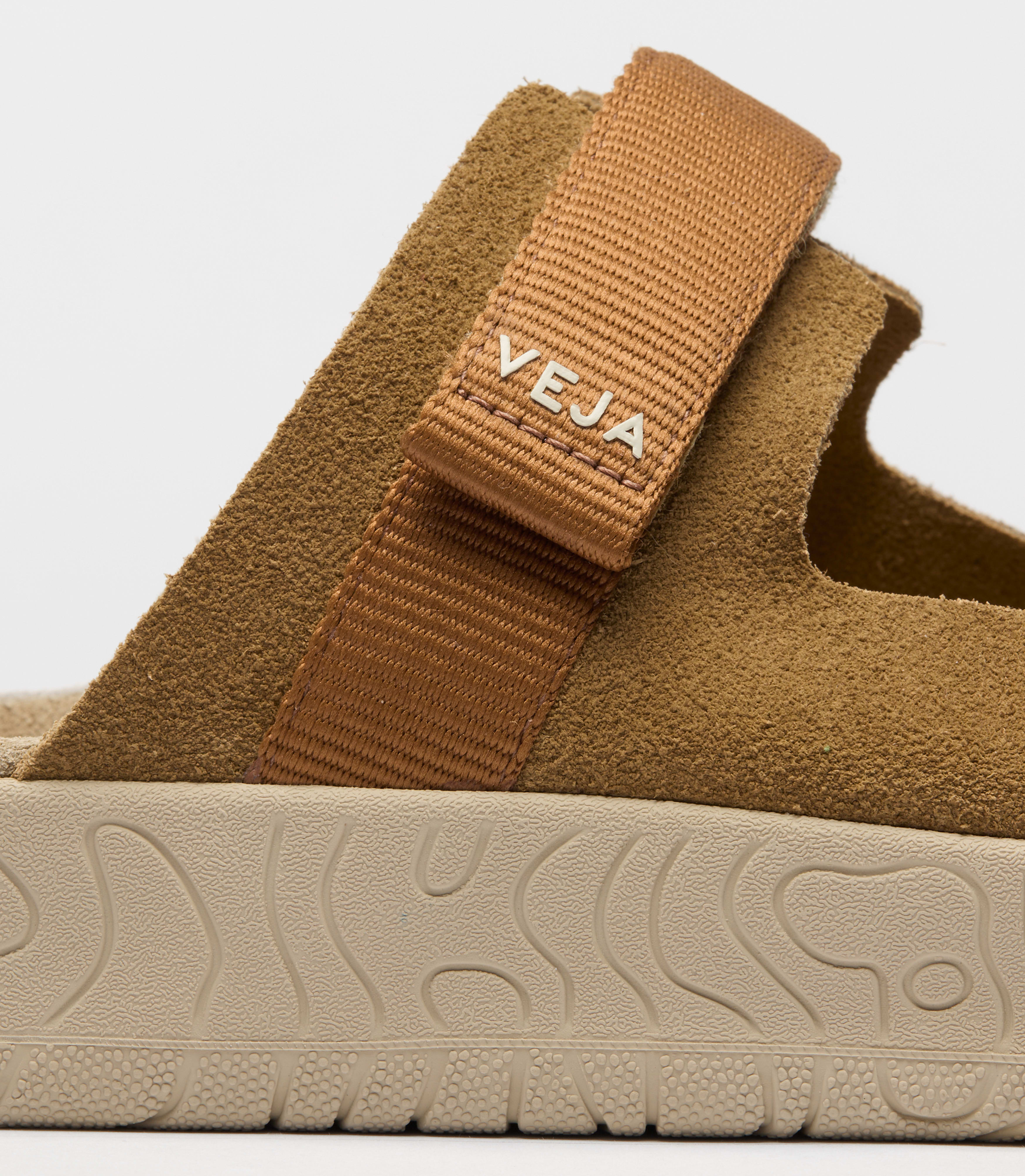 Close-up view of the Veja Arpoador slide sandal featuring cognac suede upper with tan adjustable straps set on a beige footbed and lightweight platform sole at Alas Eius.