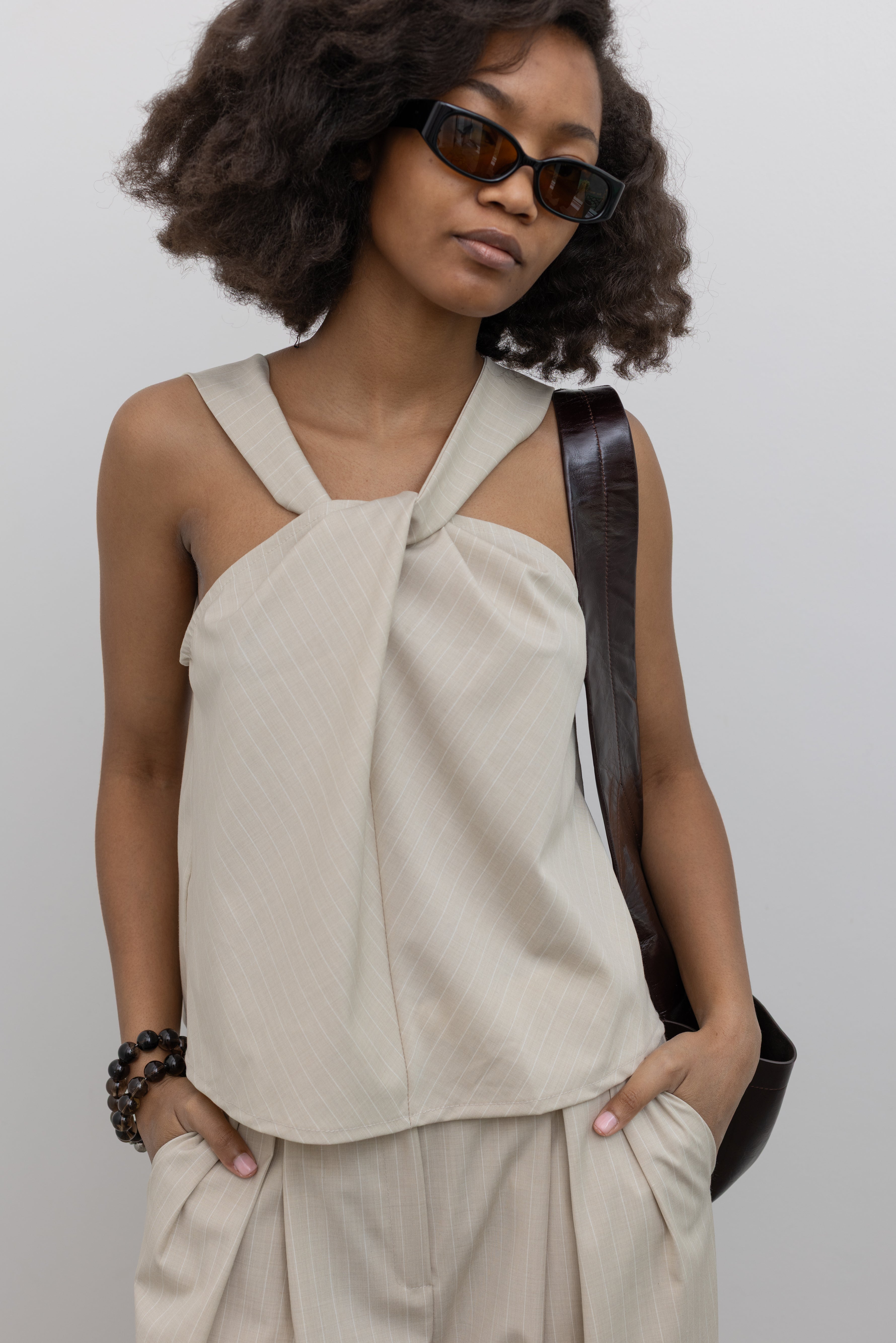 Collective sleeveless pinstripe halter top featuring sculptural front twist detail at Alas Eius