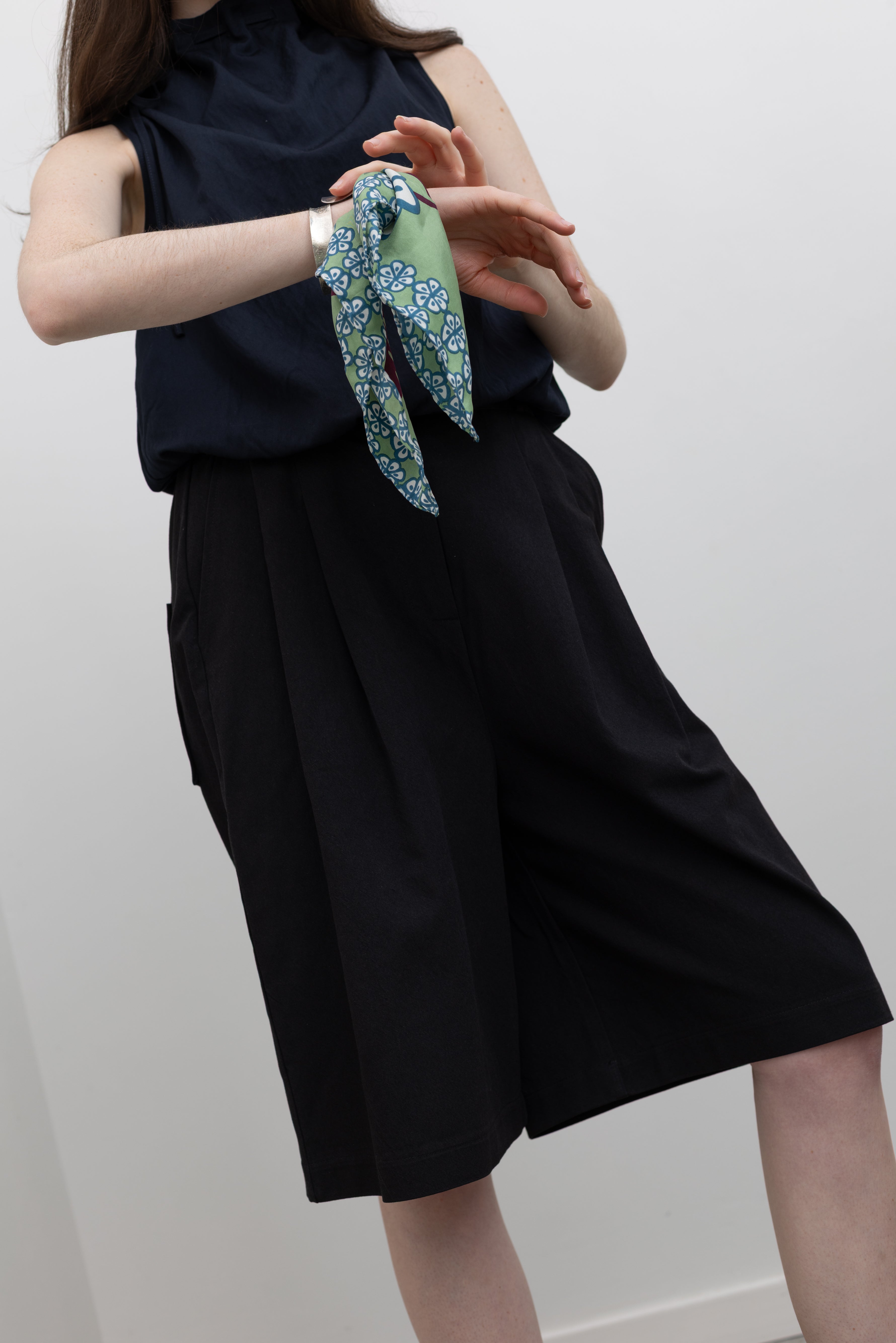 Collective tailored black shorts featuring a pleated front, elasticated back waist, and polished finish paired with a navy blue cinched mock neck top with a Les Belles Vagabondes designer silk twill scarf  with hand-printed artwork, worn as a wrist accessory for everyday styling at Alas Eius.