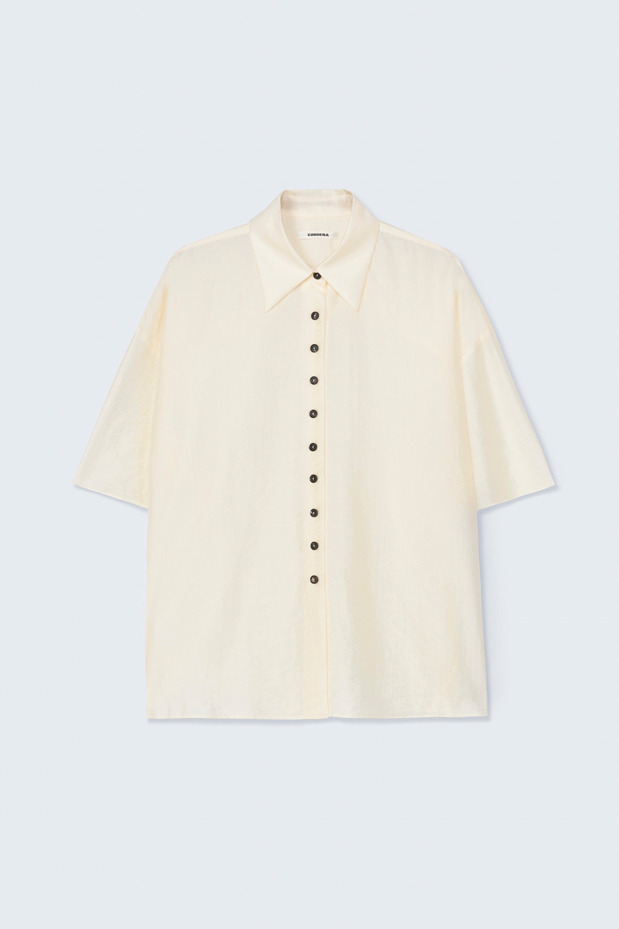Front product view of the Cordera marfil Short Sleeve Button Front Shirt featuring an oversized, cocoon-shape, roomy short sleeves, pointy collar, small contrasting buttons down the front at an Alas Eius store. Made in Spain. 