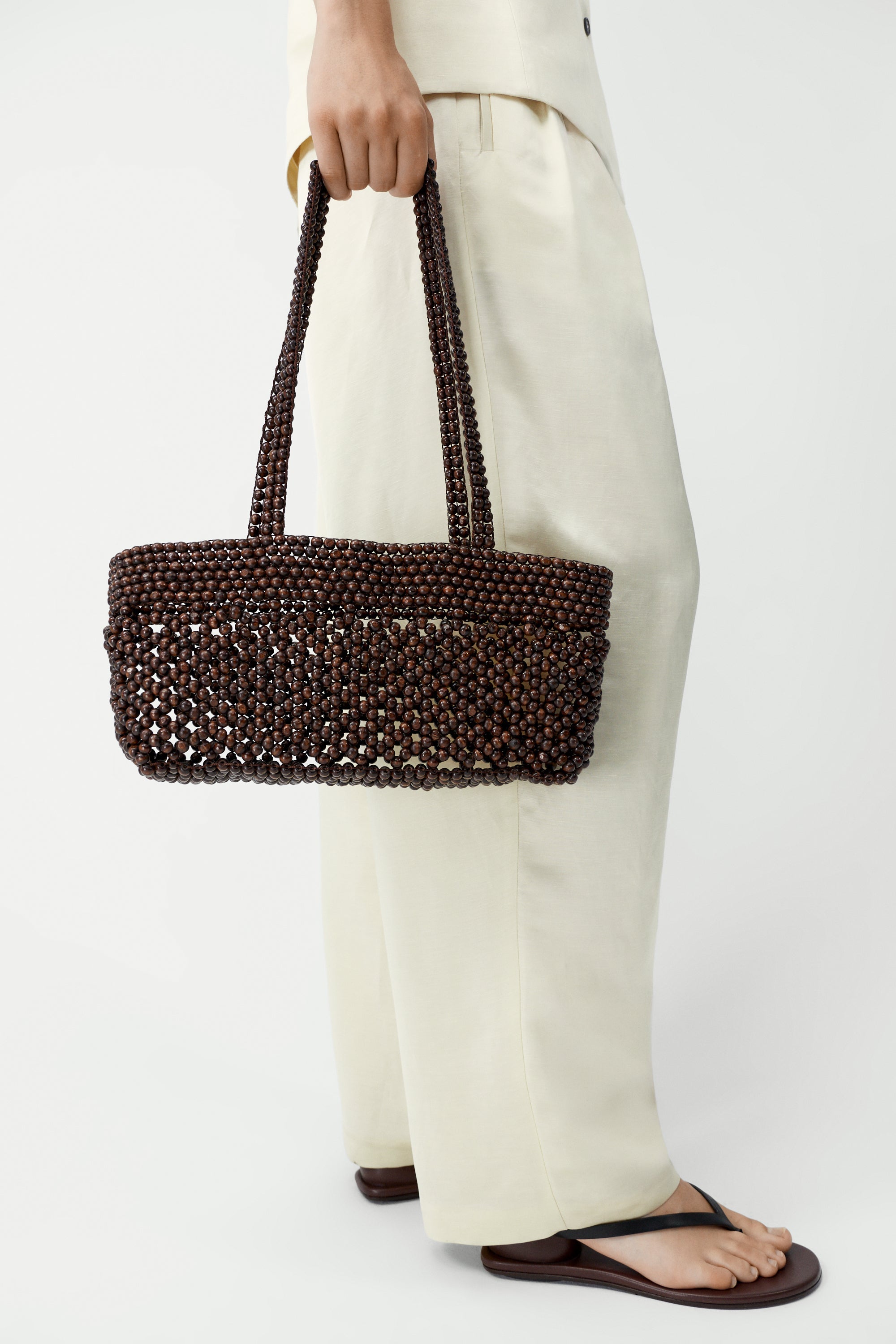 Cordera brown wooden bead mini baguette shaped bag. Adorned with natural wooden beads meticulously strung one by one and it comes with double handles for easy shoulder wear at Alas Eius. 