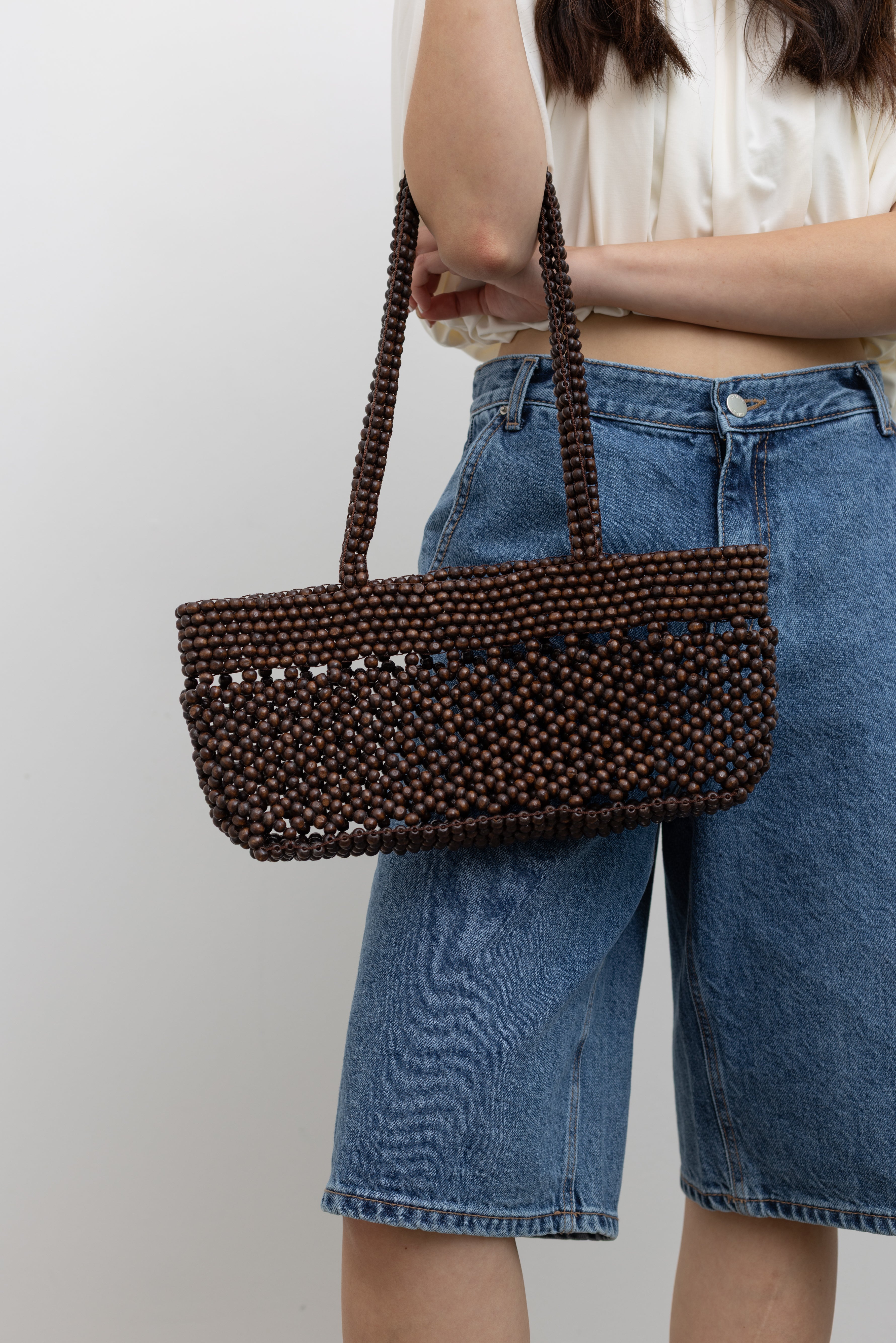 Cordera brown woven beaded shoulder bag featuring a handcrafted open-weave design, elongated shoulder straps, and a structured rectangular silhouette for an effortless minimalist aesthetic.
