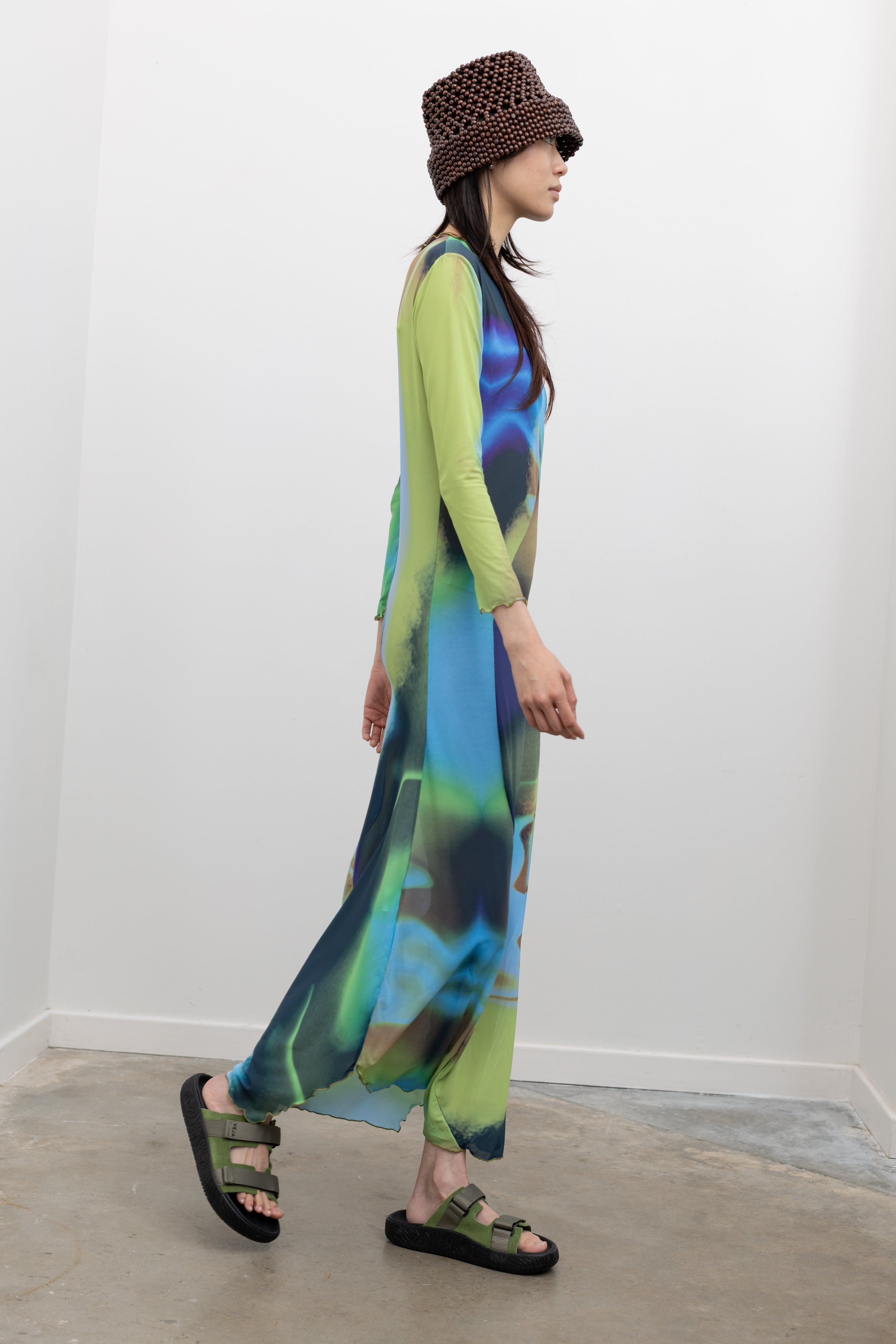 Nin Studio body-skimming long sleeve dress with bold abstract pattern, lettuce hem, and curved center detailing paired with a Cordera beaded bucket hat and Veja slide sandals at Alas Eius.