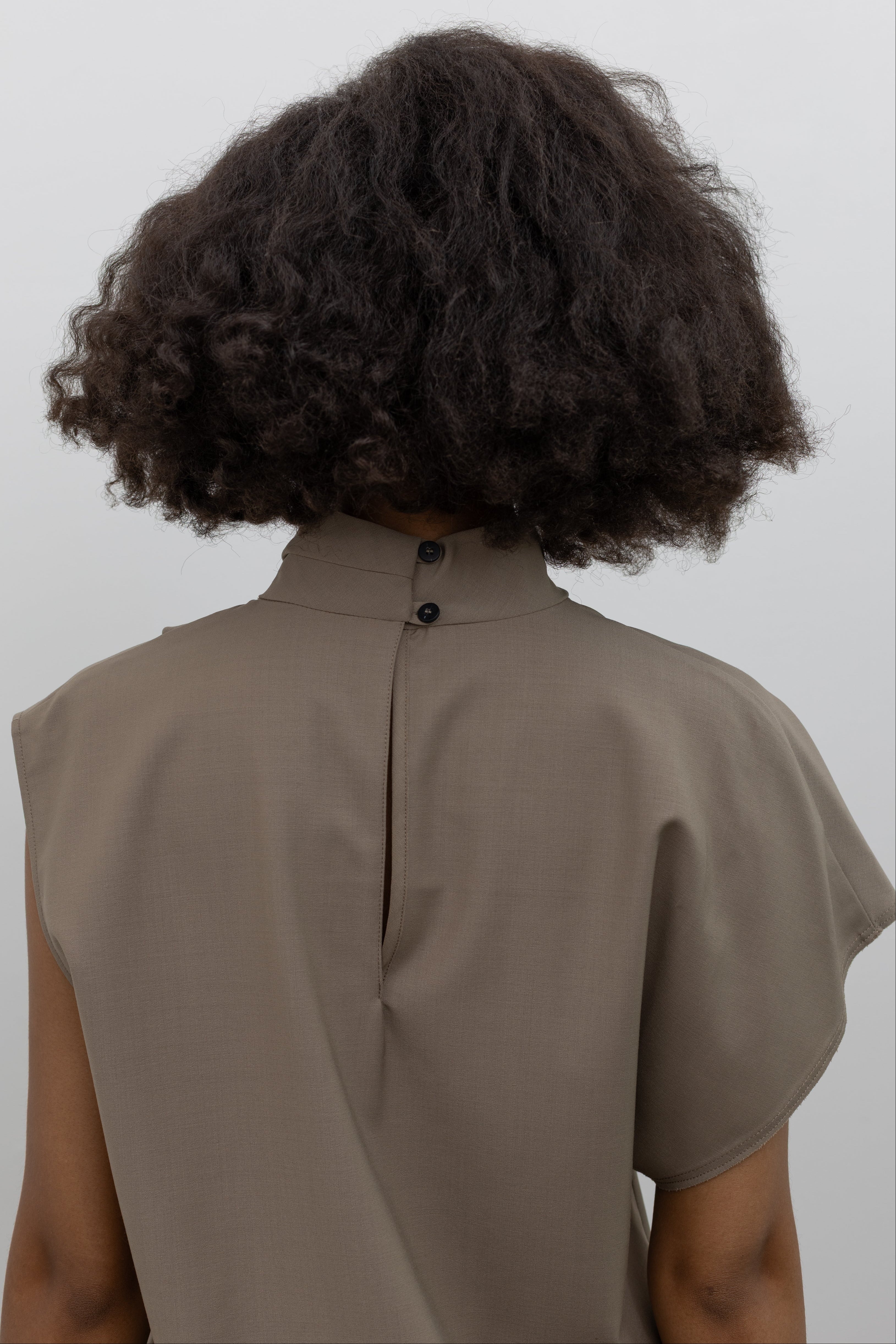 Tela elevated wool-blend top with a fluid draped front, high neckline, and modern asymmetrical sleeves at alas eius.