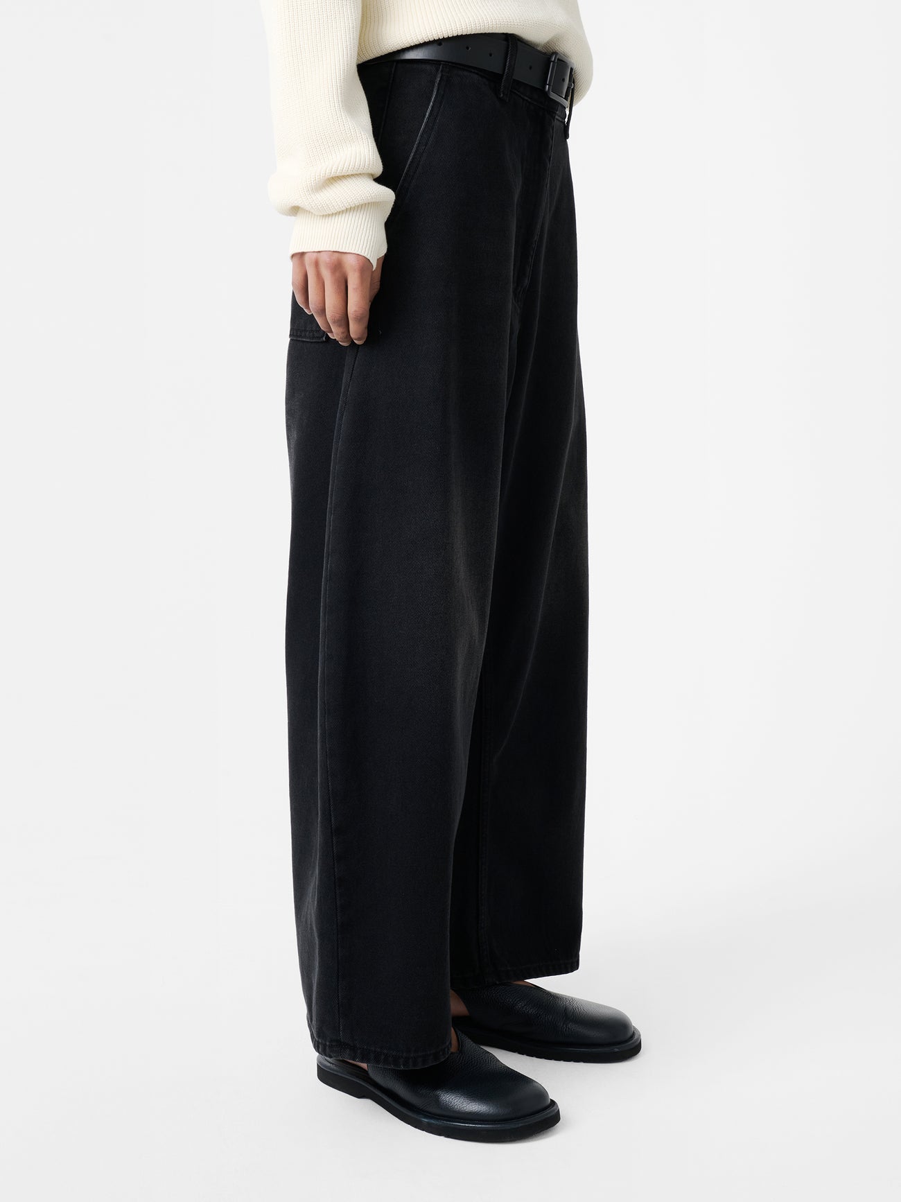 Close-up side of a woman wearing spring fashion in the Studio Nicholson Washed Black Chalco Wide Crop Denim Pant that are cut wide and cropped, with a curved leg and dropped crotch at Alas Eius. They are constructed from a denim that’s been woven from regenerative cotton and made in the UK. 